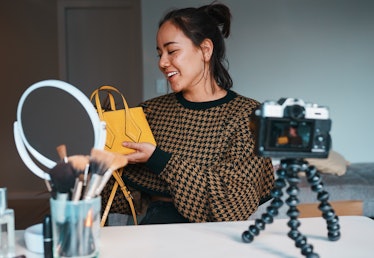 Shot of a young woman showing off a stylish bag while filming a fashion blog at home