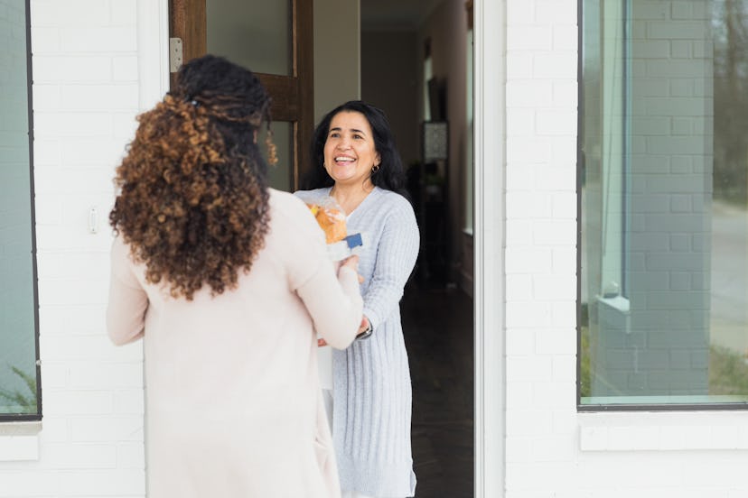 A young female grocery delivery person delivers a box filled with groceries to a mature woman.