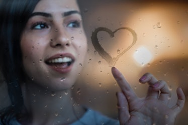 Young woman drawing heart on a foggy window