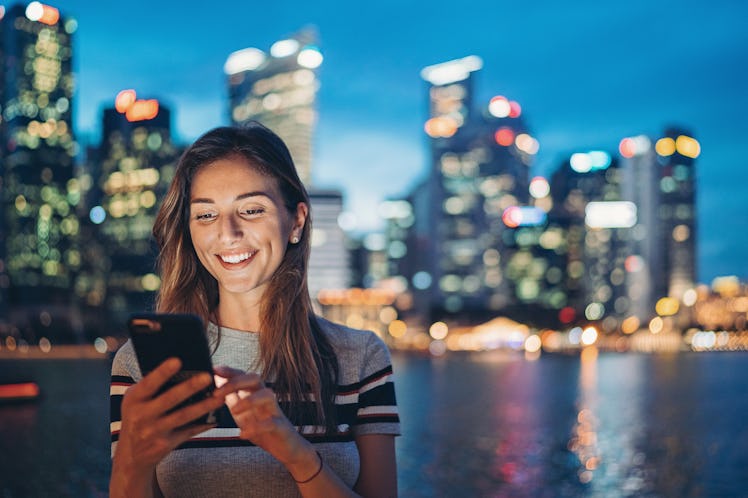 Portrait of a smiling young woman holding a cell phone outdoors in the city