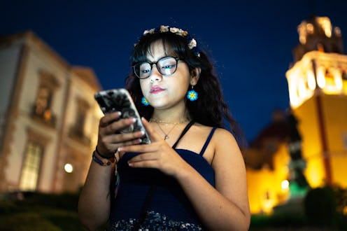 A woman looks at her phone while walking outside at night. How to ghost someone in the nicest way po...