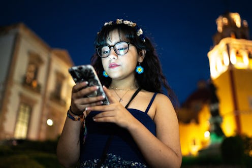 A woman looks at her phone while walking outside at night. How to ghost someone in the nicest way po...