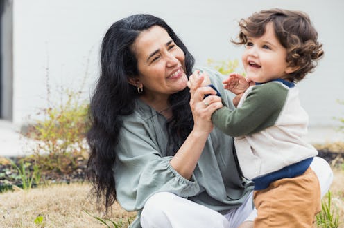 An adorable toddler boy smiles while playing outdoors with his beautiful grandmother.