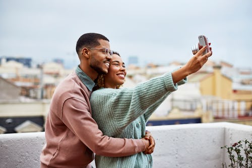 Smiling young woman taking selfie with boyfriend at building terrace. Cancer and Virgo compatibility...