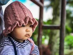 Close up of a baby wearing a pink knit beanie, in a story about Capricorn girl names.