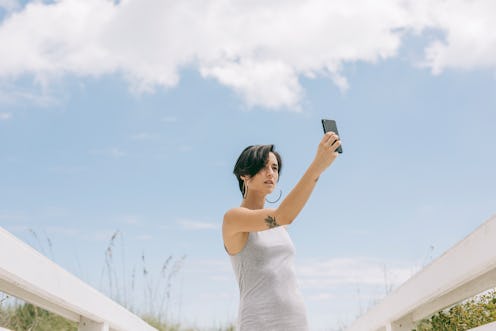 Young woman taking a self portrait at the beach. Apple's new privacy feature in iOS 14.5 lets you st...