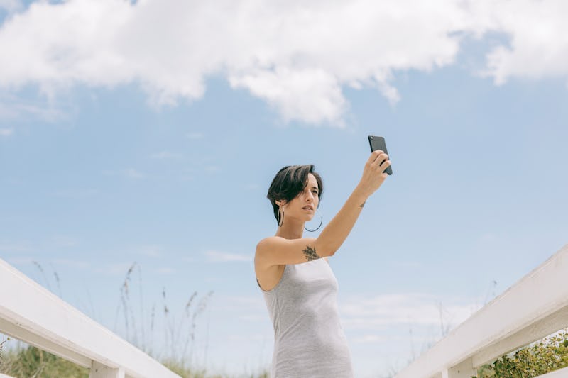 Young woman taking a self portrait at the beach. Apple's new privacy feature in iOS 14.5 lets you st...