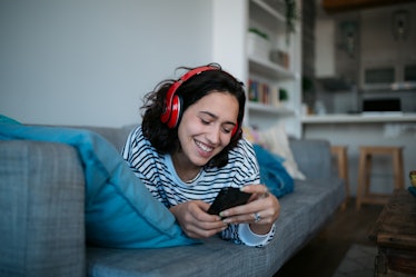 Happy Caucasian woman relaxing at home, smiling and listening to music using headphones and a smart ...