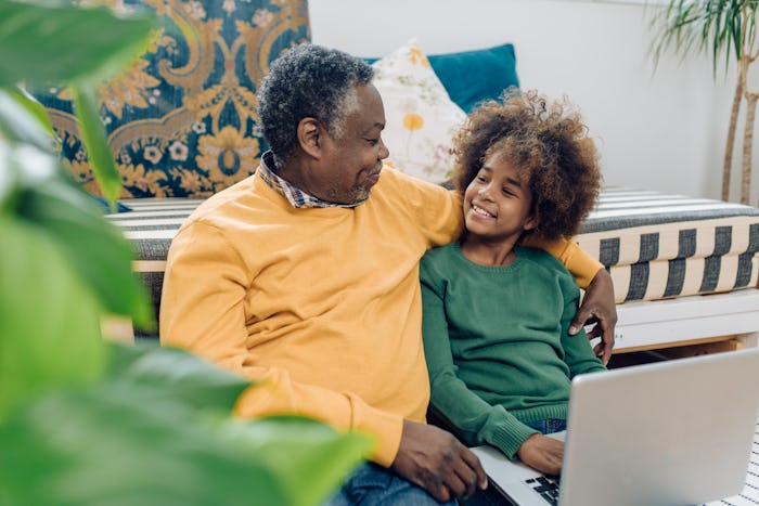 African American teenage girl enjoying at home with grandpa and using a laptop.