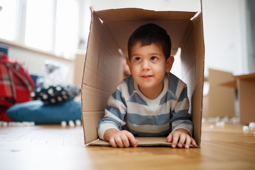 Charming toddler smiling and looking up, lying on front in empty box on the floor during house move