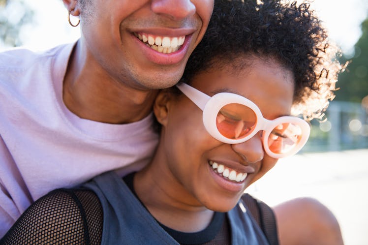 A close up of a fashionable young African American couple leaning on each other and smiling outdoors