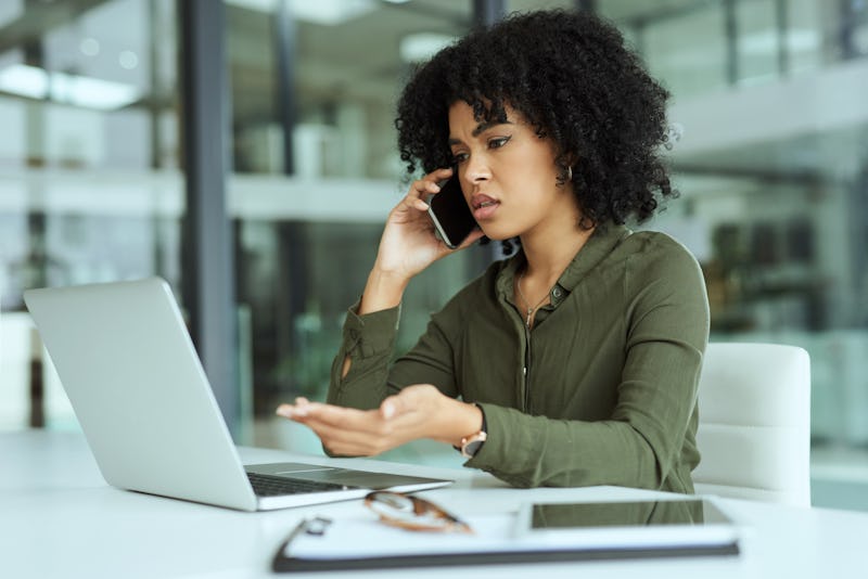 Shot of a young businesswoman looking stressed while using a laptop and smartphone in a modern offic...