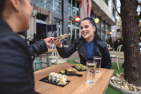 Two young women sitting in restaurant, eating sushi and talking