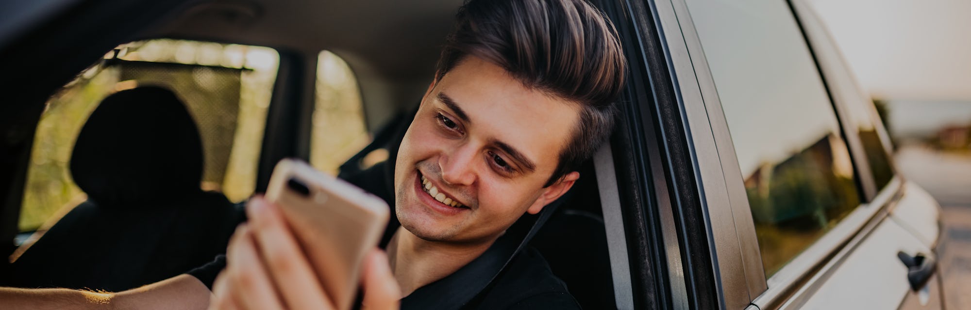 Young, handsome man pulled over with his car and making video call on phone.