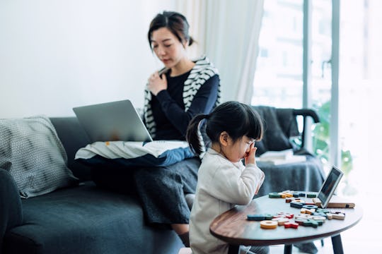 Exhausted young Asian mother and little daughter rubbing tired eyes while working from home on lapto...