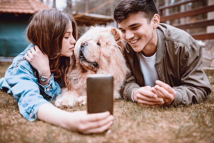 A happy couple takes a selfie in the backyard with their dog.
