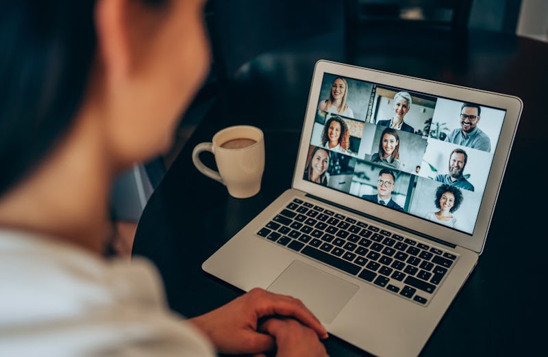 A person sits on a video conference call on their laptop with coffee on the table next to the comput...