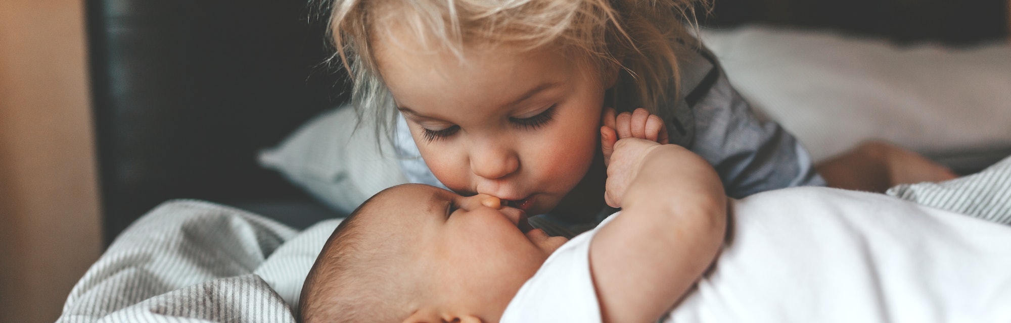 Little brother hugging his newborn sister. Toddler kid meeting new sibling. Cute boy and new born ba...
