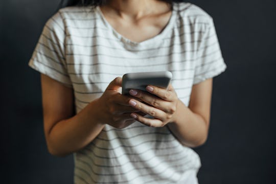 An unrecognizable woman dressed in a white T-shirt with black stripes texting on her smartphone.