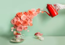 Buttler hand with glove pouring a stream of roses into tea cup on green background. Surreal conceptu...