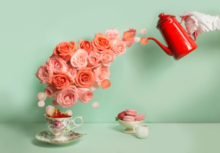 Buttler hand with glove pouring a stream of roses into tea cup on green background. Surreal conceptu...