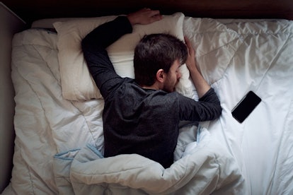 Young male sleeping in the bed only himself during the day smartphone next to him