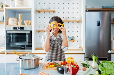 A smiling young woman looks through bell pepper slices in kitchen at home while recreating a TikTok ...