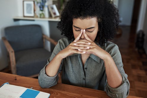 A person puts their index fingers to their temple and closes their eyes while working from home. Anx...