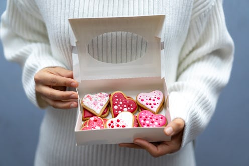 Woman wearing white sweatshirt holding a box with Valentine's cookies in heart forms