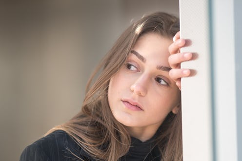 Close up of the head and face of a tired, worried, pensive woman resting her head and nah on a wall ...