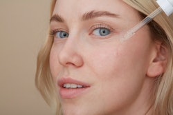 A close-up of a woman applying over-the-counter retinoids on her face with a dropper