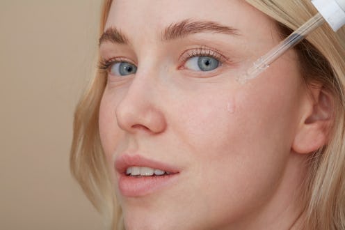 A close-up of a woman applying over-the-counter retinoids on her face with a dropper