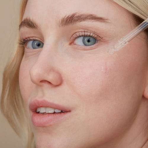 A close-up of a woman applying over-the-counter retinoids on her face with a dropper
