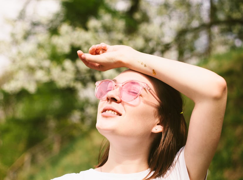 Woman wearing white t-shirt and pink sunglasses relaxing in spring park. Outdoors portrait of young ...