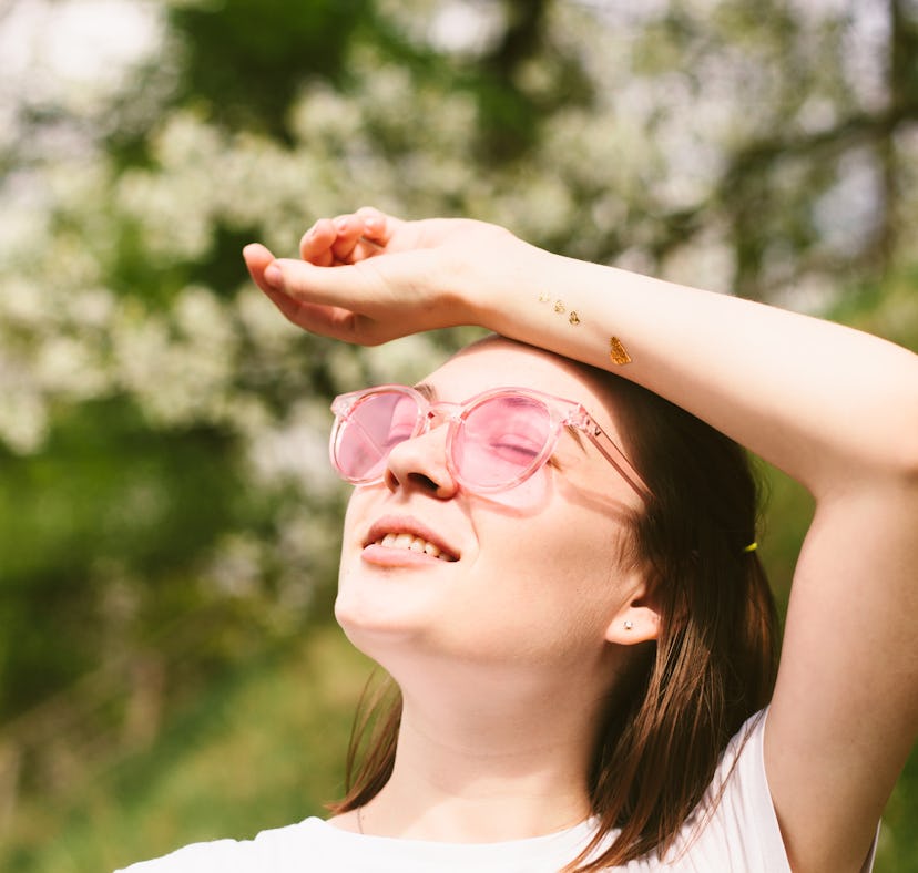 Woman wearing white t-shirt and pink sunglasses relaxing in spring park. Outdoors portrait of young ...