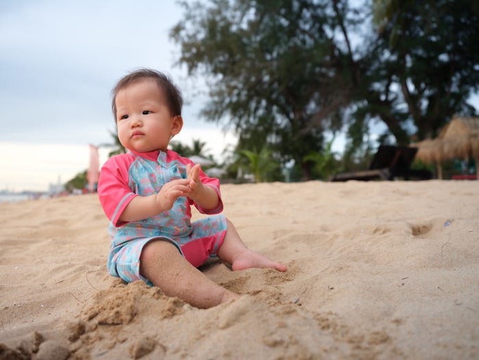 Baby experiencing the beach for the very first time. Mother guiding her baby through her sand and wa...