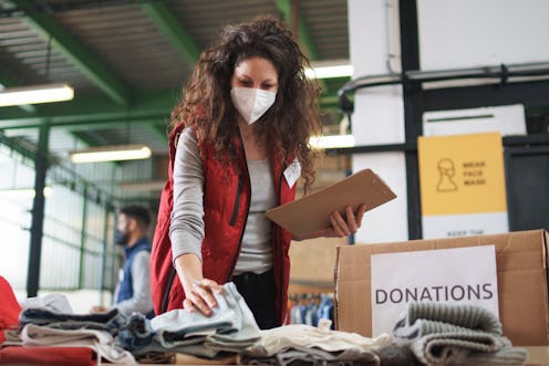 Woman with face mask sorting clothes while volunteering to help people affected by the coronavirus p...