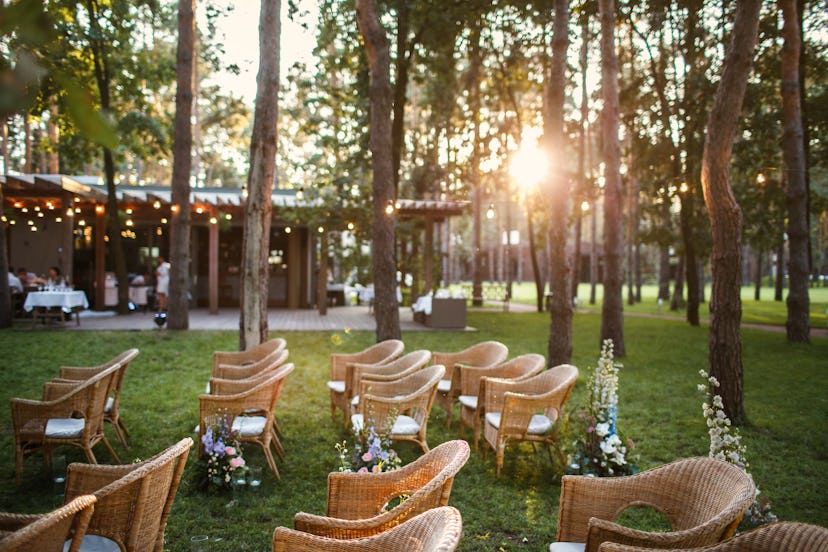 Place of the wedding ceremony at sunset in the open air. Wicker chairs stand under luminous yellow l...