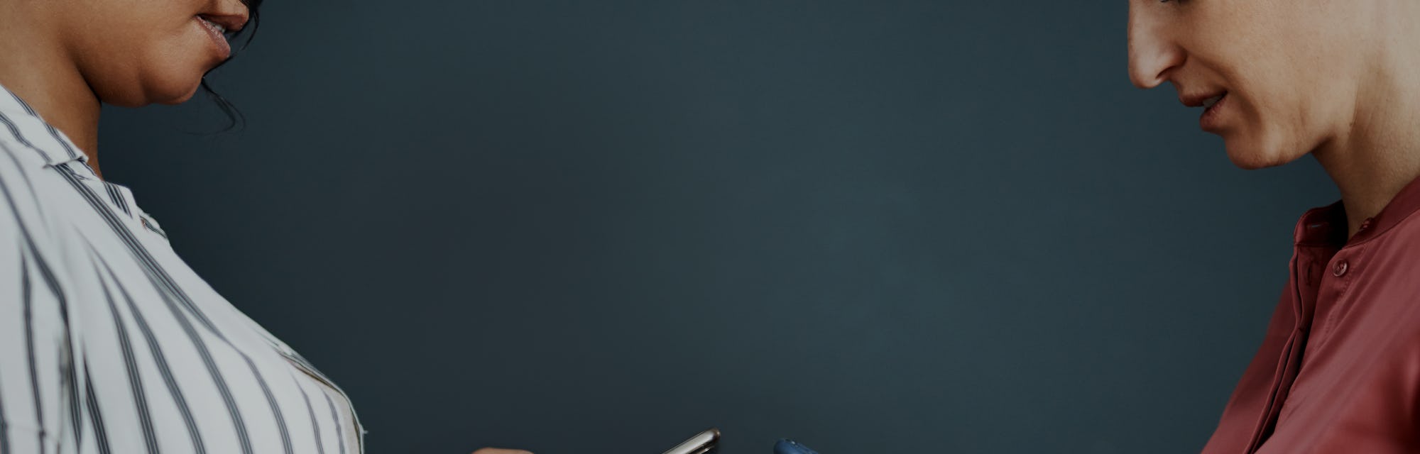 Cropped shot of two attractive young businesswomen standing against a gray background and texting on...