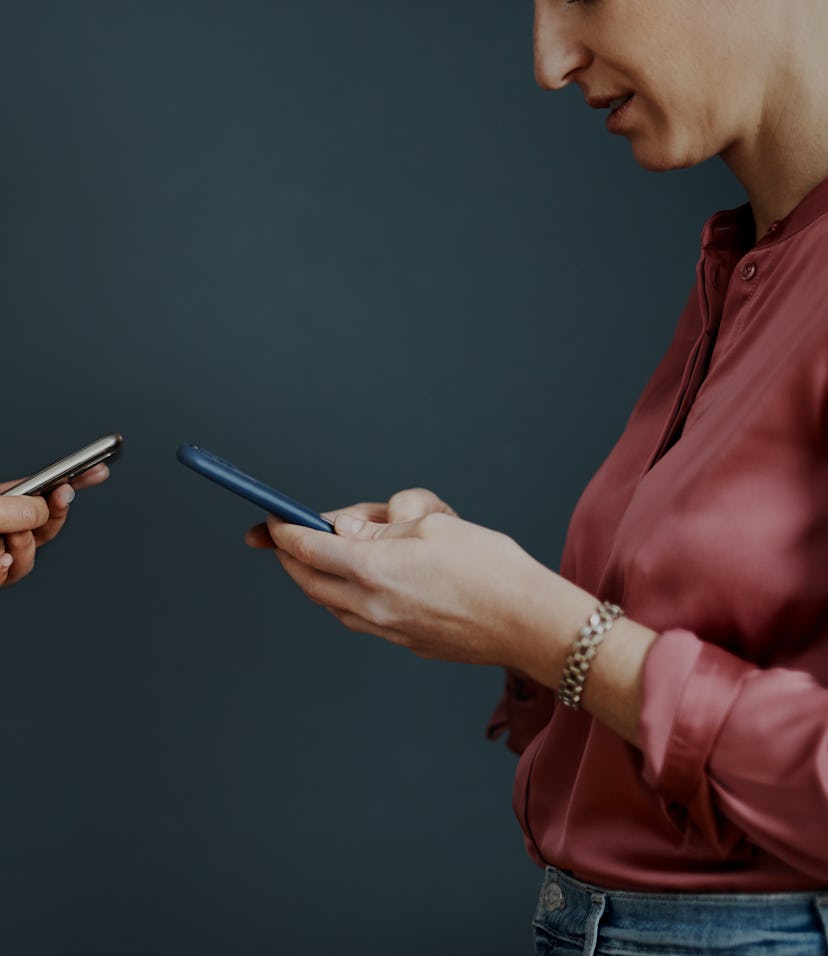 Cropped shot of two attractive young businesswomen standing against a gray background and texting on...