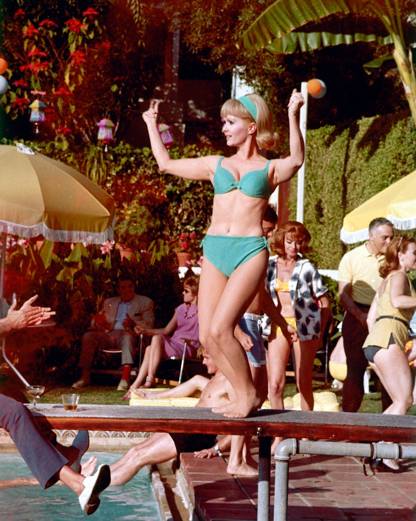Debbie Reynolds wearing a blue bikini while dancing on a diving board over a swimming pool, circa 19...