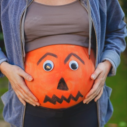 Pregnant woman  with her belly painted in orange  and eyes as a  halloween pumpkin.