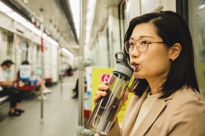 asian businesswoman drinking water from a reusable water bottle in the subway