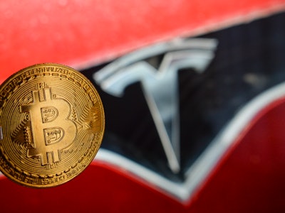 Illustrative image of a commemorative bitcoin in front of the Tesla car logo.
Tesla, led by Elon Mus...