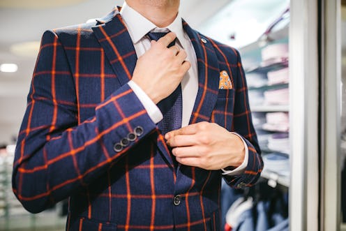 Young caucasian man trying suit and adjusting necktie in suit shop.