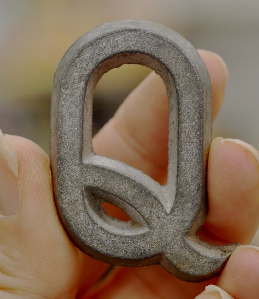 Caucasian female hand holding up a metal capital Q