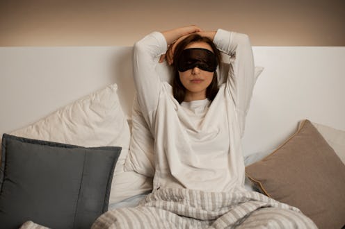 A woman with her hands above her head and a black sleeping mask over her eyes before sleep