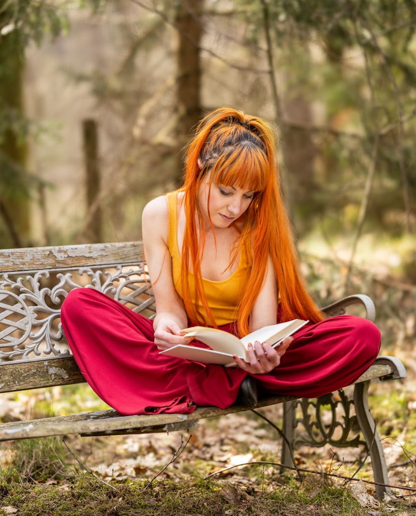 Young woman sitting on a bench in nature, relaxing and reading a classical book novel.