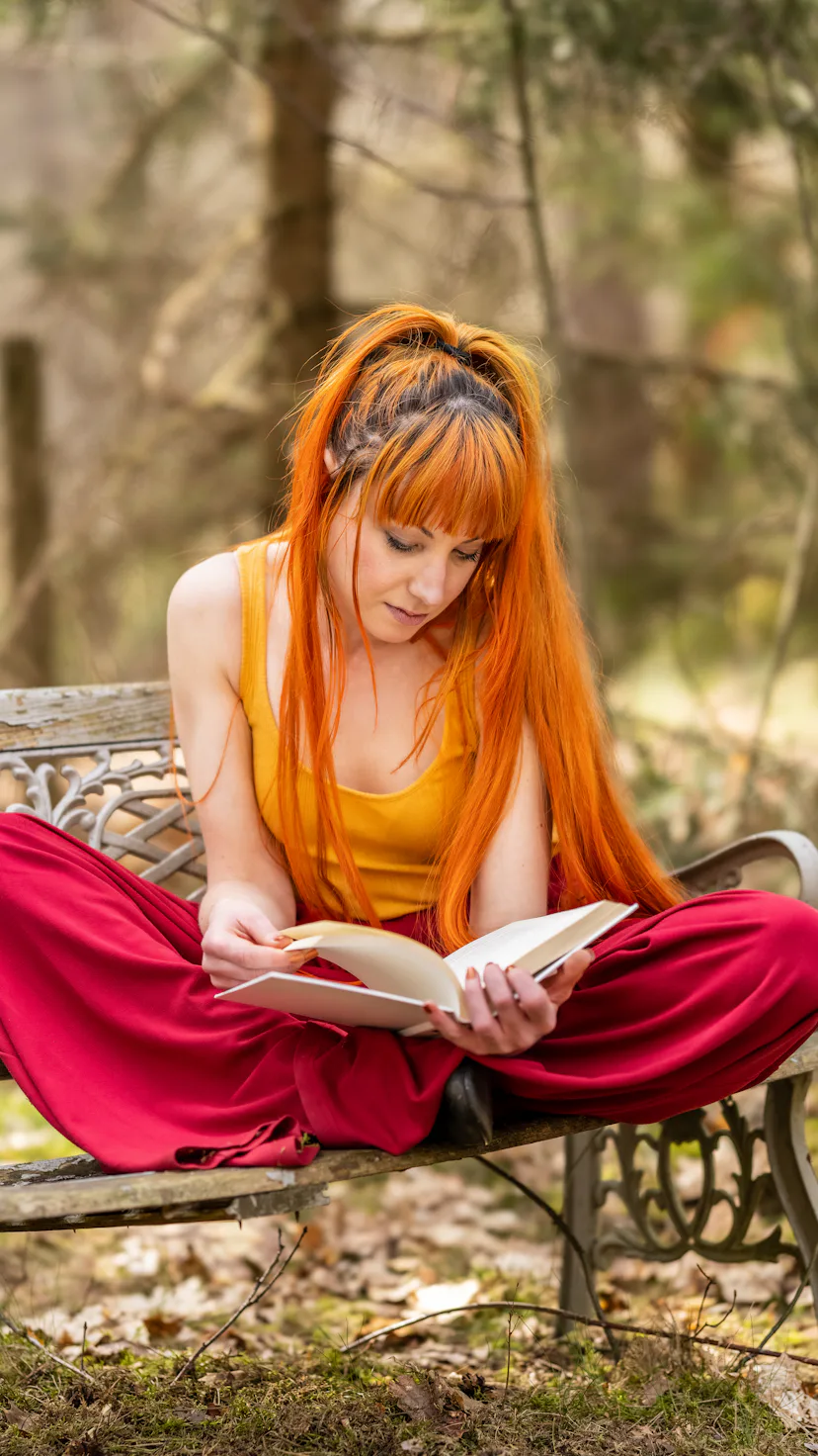 Young woman sitting on a bench in nature, relaxing and reading a classical book novel.