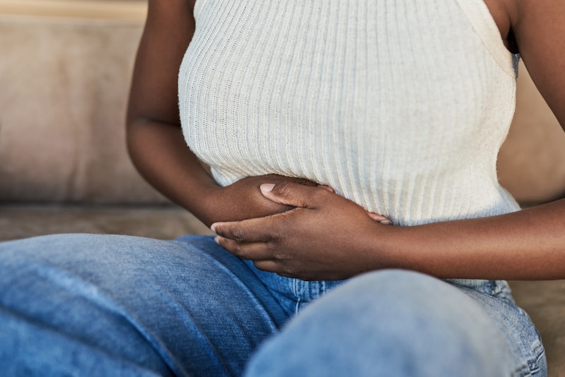 A woman wearing a white shirt and jeans holds her stomach, wondering if she might be pregnant. Among...